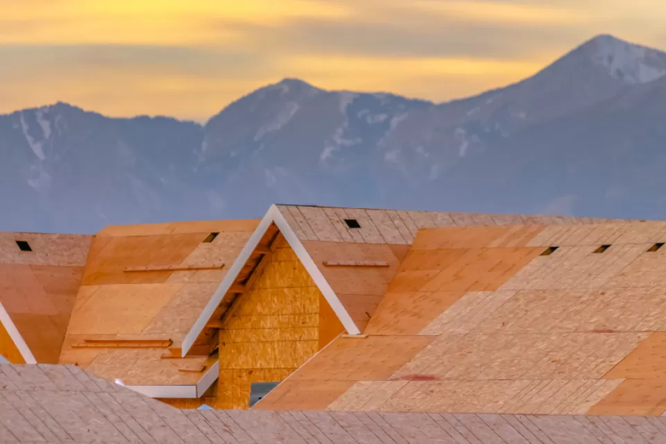 Close-up of wood-frame houses under construction with mountains in the background against sunset sky